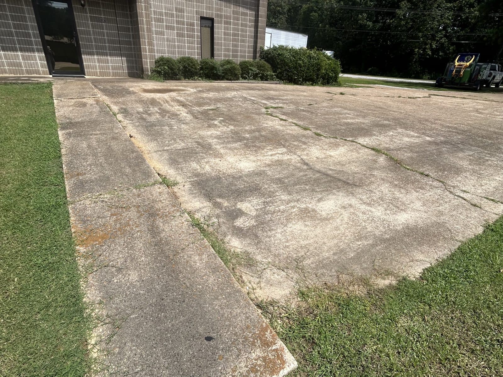 Weathered concrete pad beside a commercial building, streaked and darkened before pressure washing